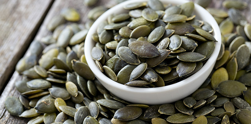 A bowl of pumpkin seeds with some of the table beside